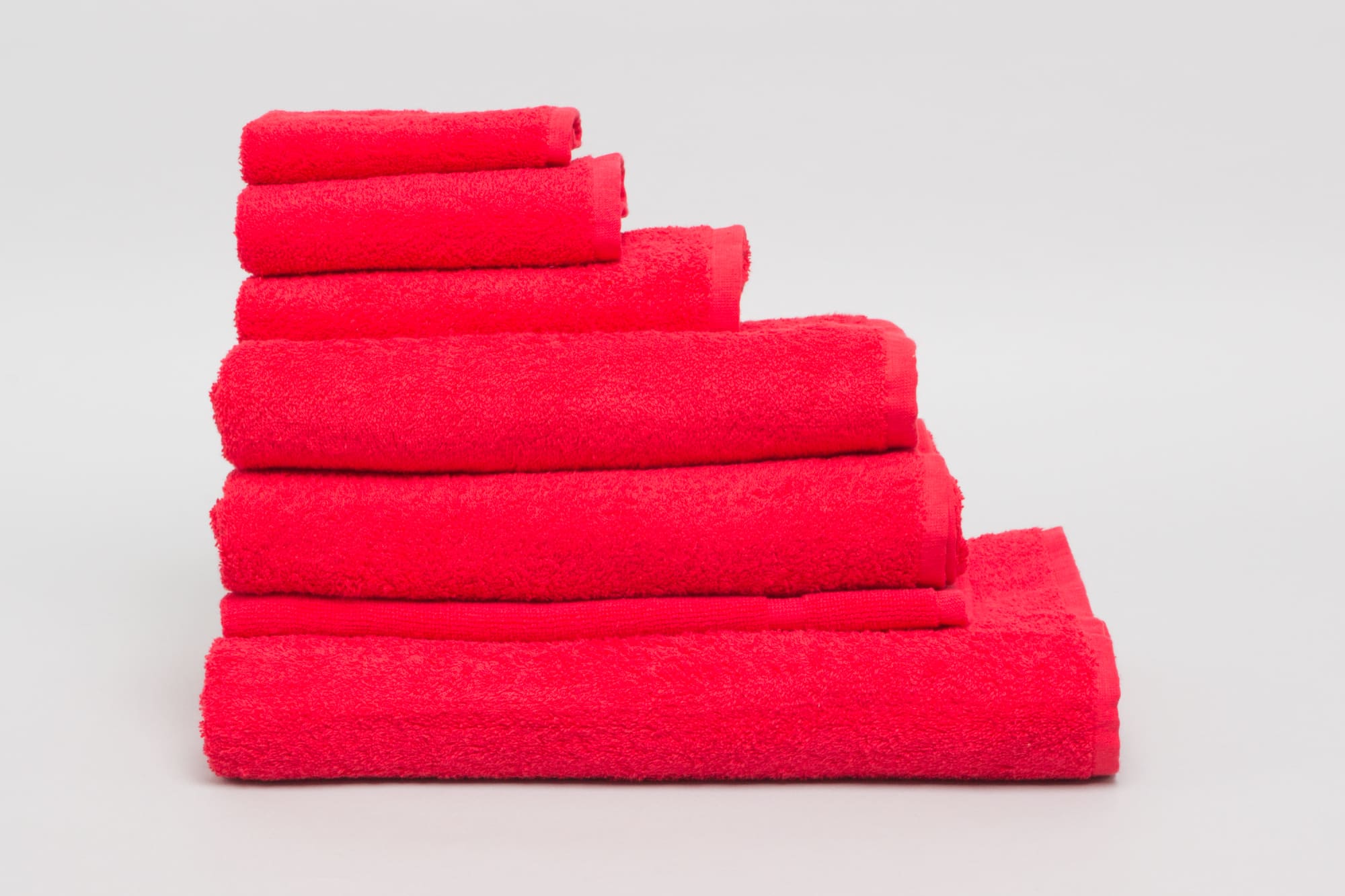 A stack of red bath towels in various sizes, showcasing a plush texture. The image includes a logo. Elite Large Hand Towel 500 gsm Red - Image 1