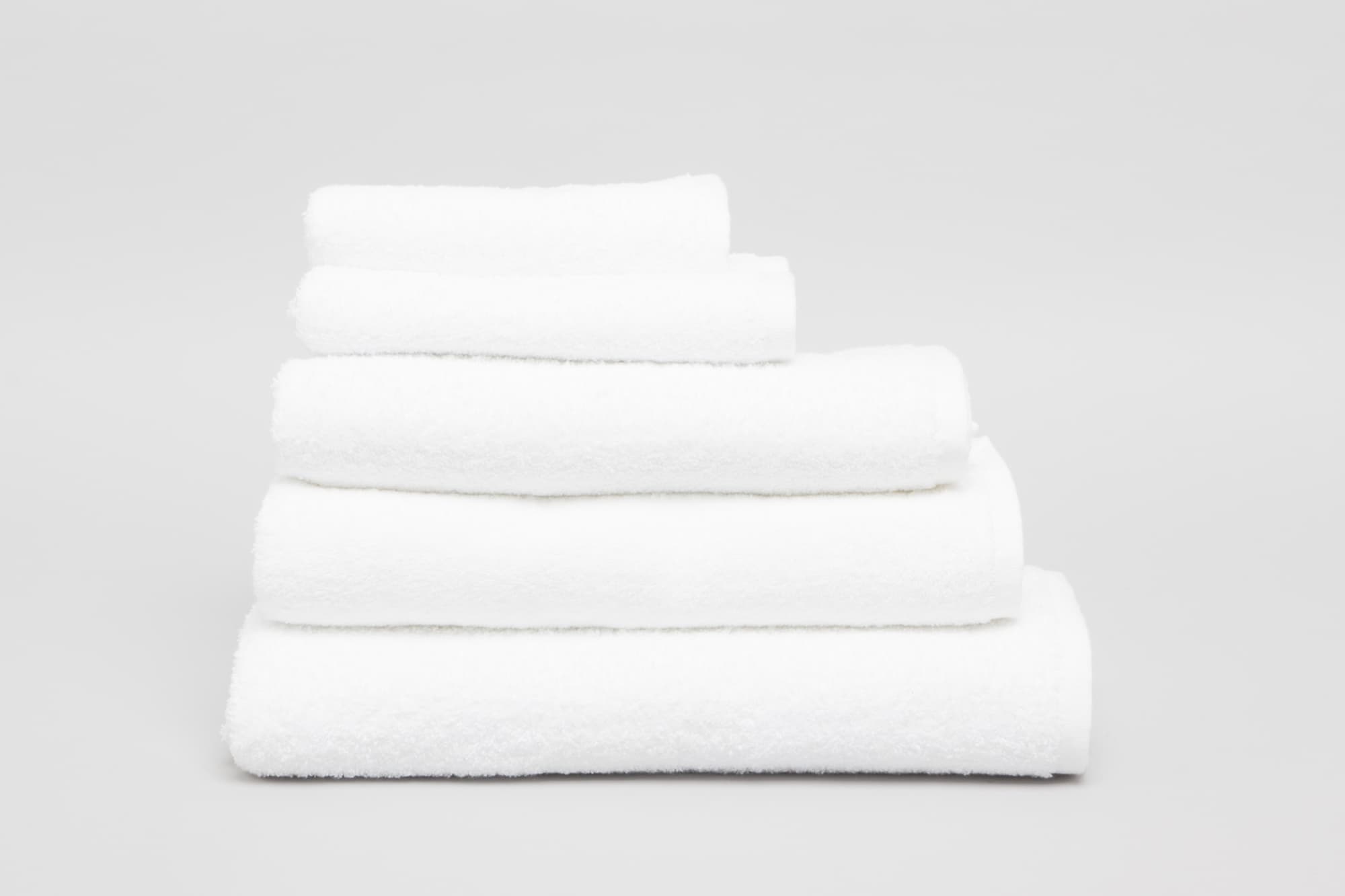 A stack of five white towels in varying sizes, showcasing their soft, fluffy texture. The image features a simple background. Elite Mega Towel 500 gsm White - Image 1