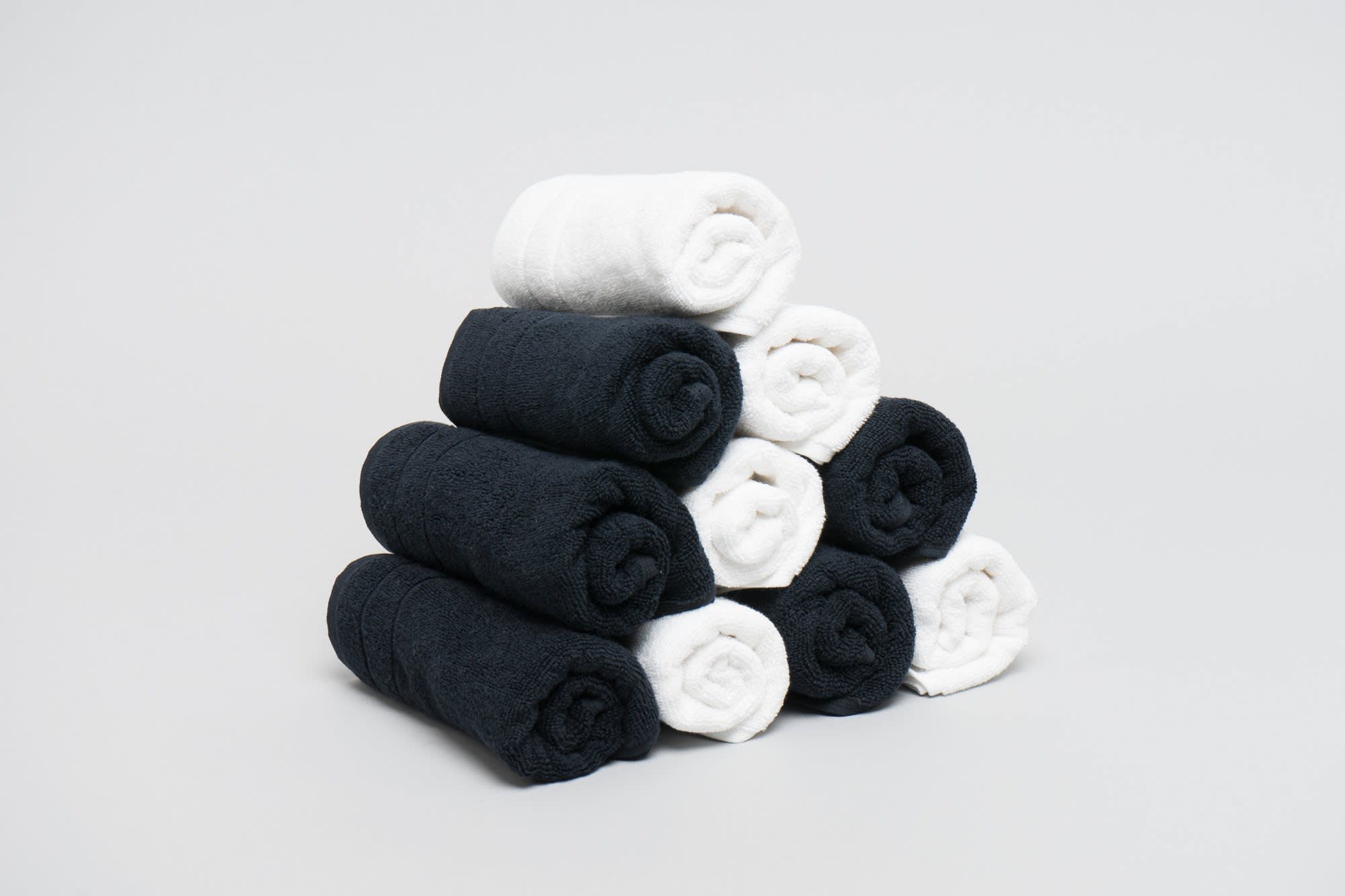 A stack of rolled towels in black and white, arranged in a pyramid shape against a light background. Excel Salon Towel 475 gsm Black - Image 1