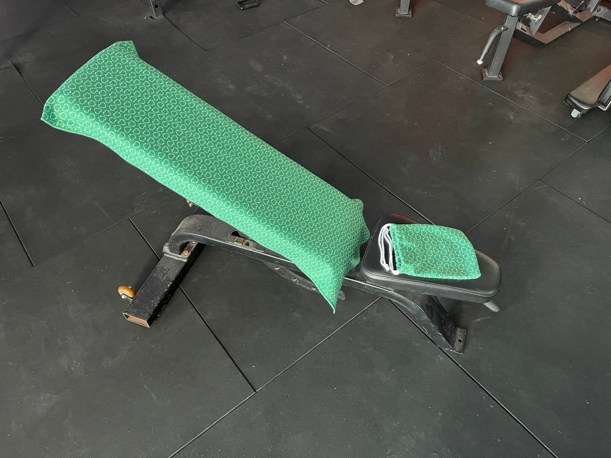 A gym bench covered with a green patterned towel. The towel drapes over the backrest and seat area. rPET Hooded Gym Towel - Image 1