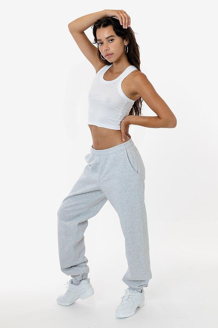 A model poses in grey heavy fleece sweatpants, paired with a cropped white tank top and white sneakers. Heavy Fleece Sweatpant - Image 1