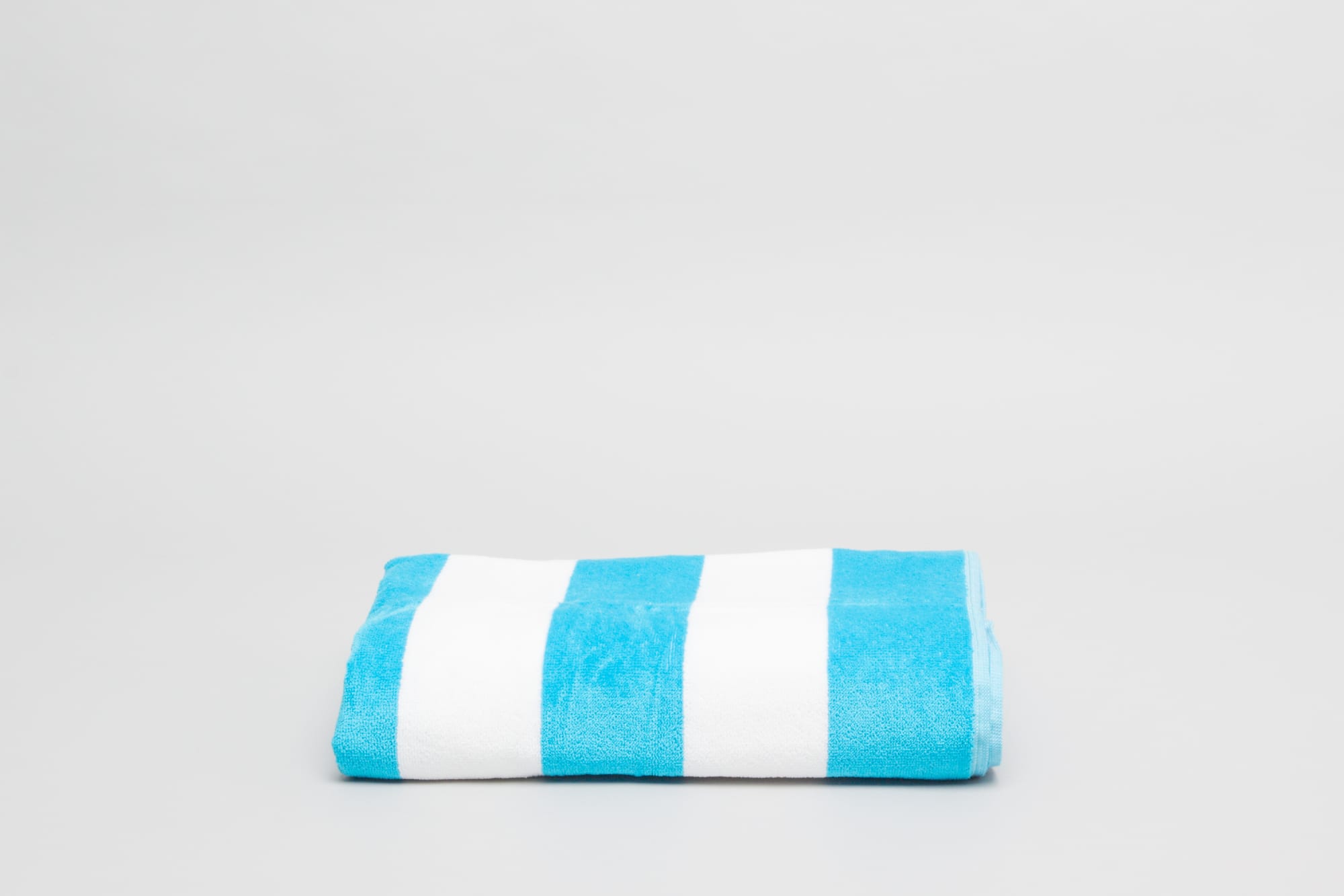 A folded aqua beach and pool towel featuring alternating white and aqua stripes, with a soft texture. Havana Beach & Pool Towel 450 gsm Aqua - Image 1