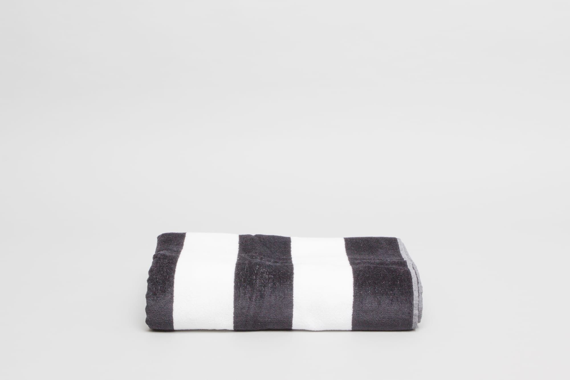 A folded towel featuring black and white stripes, showcasing a soft texture. Includes a logo. Havana Beach & Pool Towel 450 gsm Black - Image 1