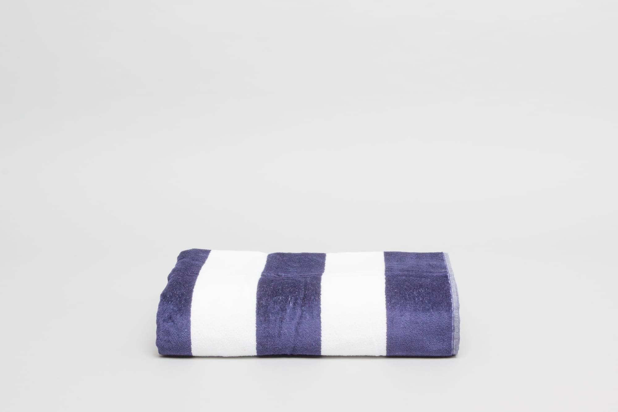 A folded beach towel featuring navy blue and white stripes, made of 450 gsm fabric. It has a logo on it. Havana Beach & Pool Towel 450 gsm Royal - Image 1