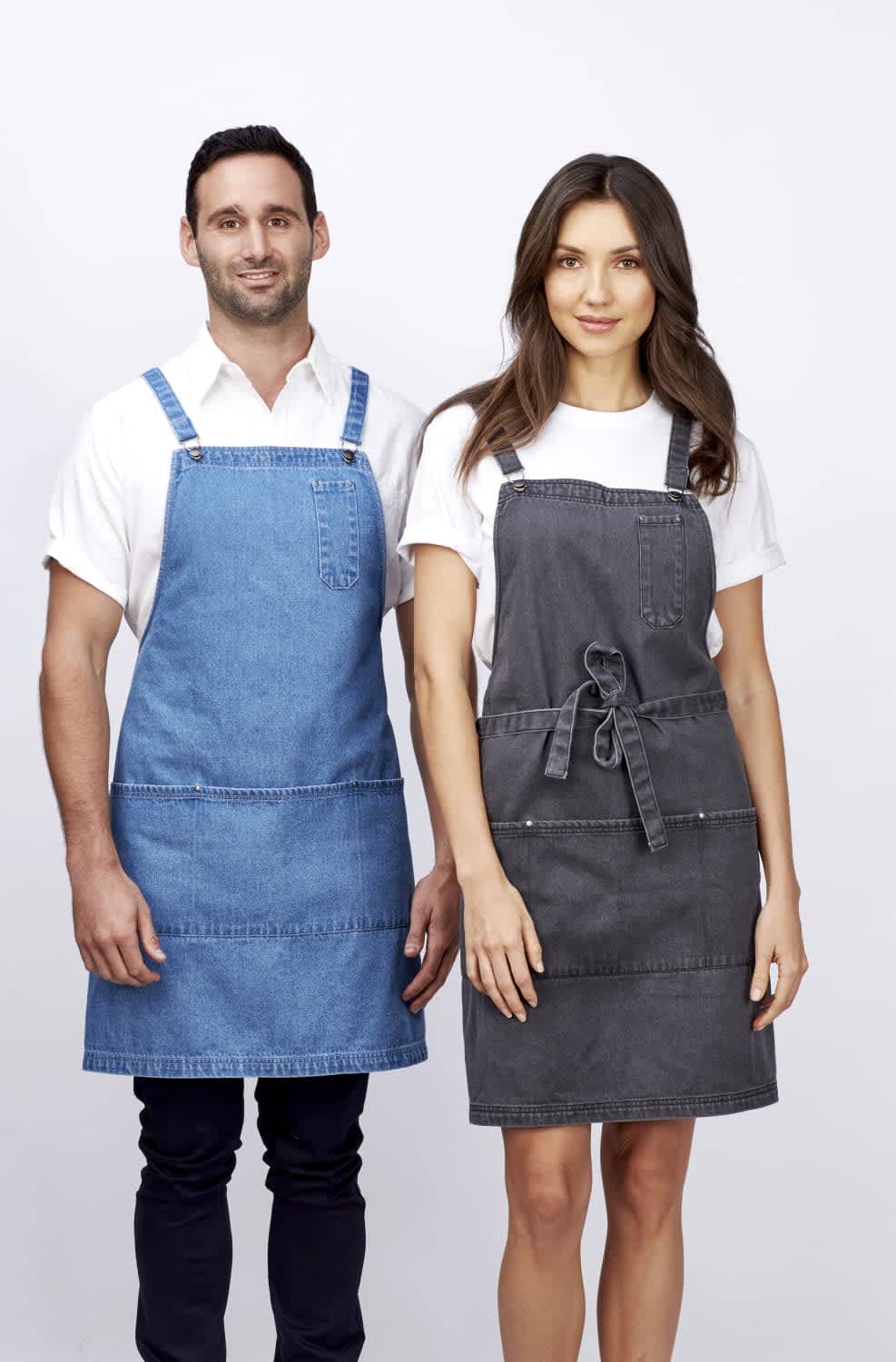 A denim bib apron in blue on a man and a grey apron on a woman, both featuring pockets and ties. Louie - Bib Apron - Image 1