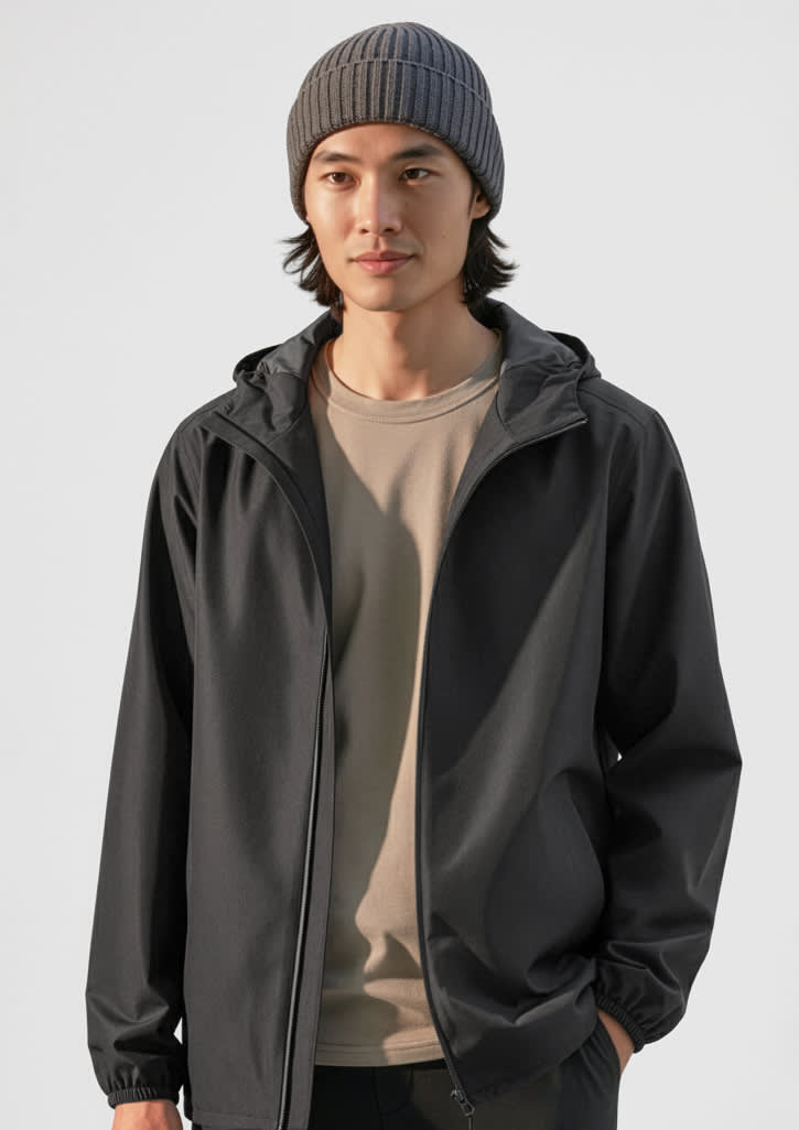 A grey rain jacket is worn by a person with dark hair, complemented by a grey beanie and a beige shirt underneath. Mens Tempest Jacket - Image 1