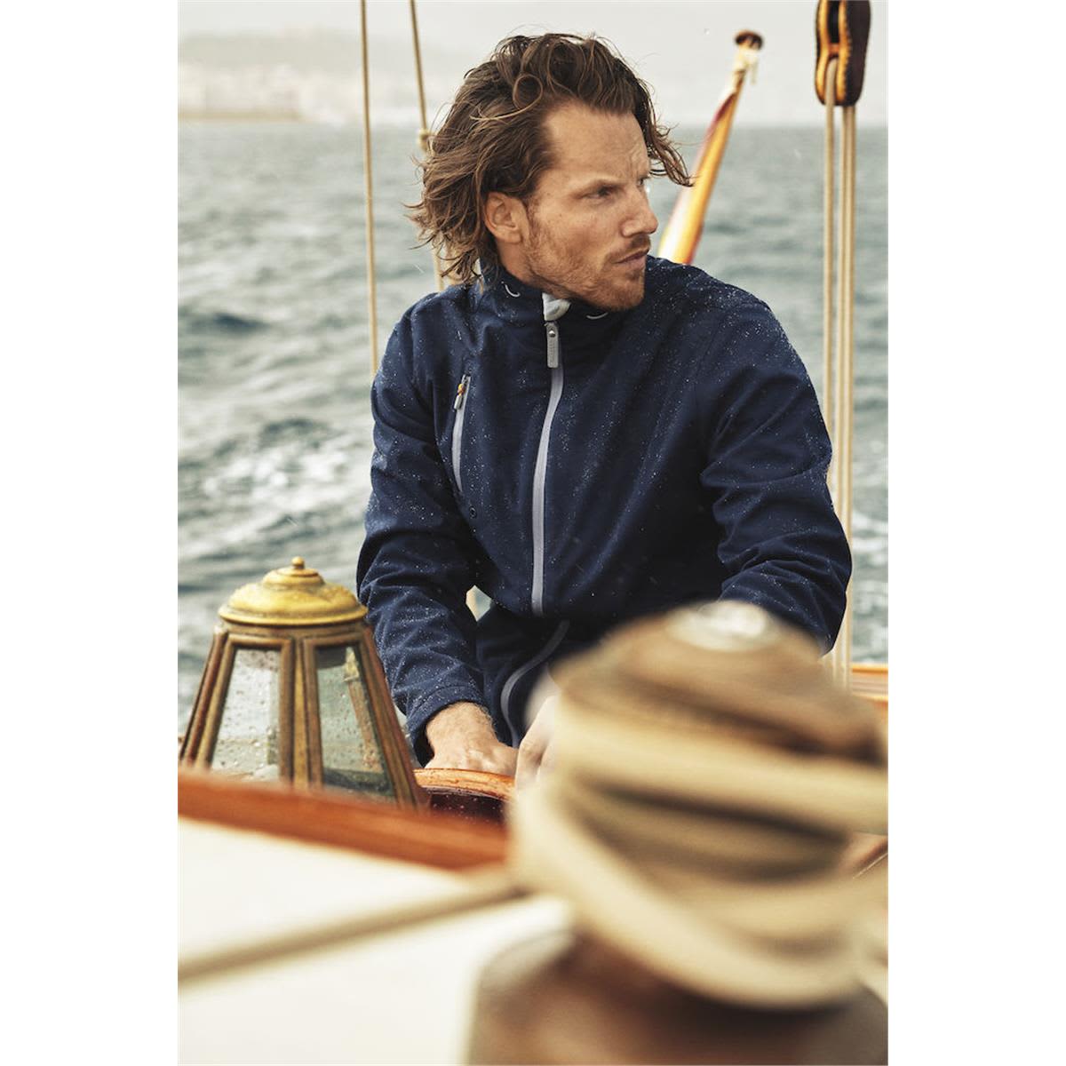 A navy softshell jacket is worn by a man sailing on a boat, with water and a coastline in the background. Snyder Men's Softshell - Image 1