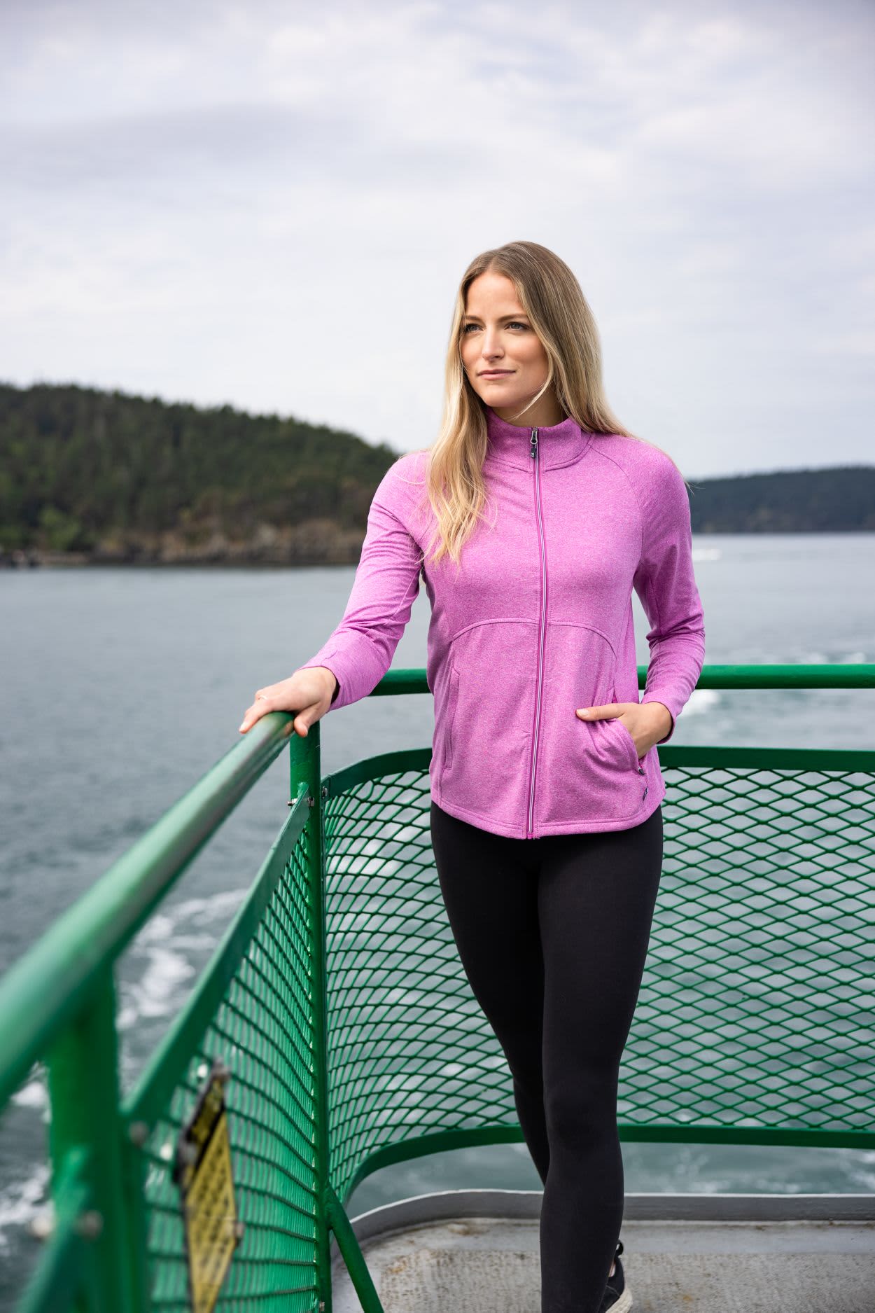 A woman stands on a boat wearing a pink full zip jacket and black leggings, with water and trees in the background. Ladies Adapt Eco Heather Full Zip - Image 1
