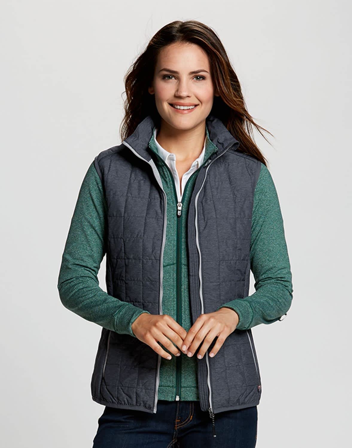 A woman wears a grey puffer vest over a green top, featuring a branding logo on the vest. CB WeatherTec Ladies Rainier Vest - Image 1