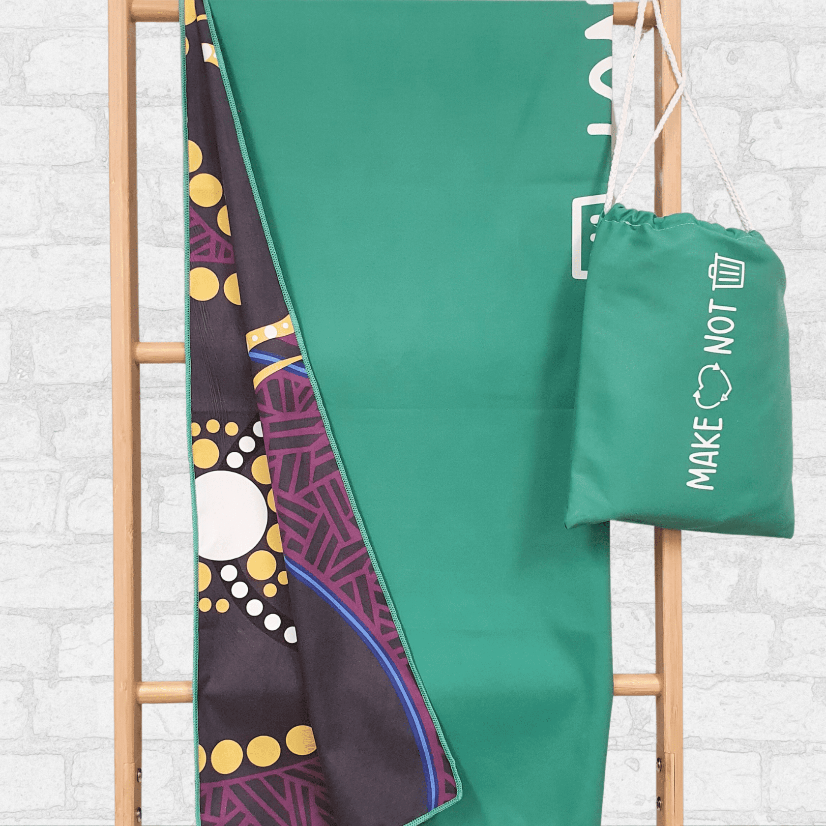 A lightweight green suede towel hangs on a wooden rack, showing a patterned underside and a matching carry bag. Lightweight Suede Sand Free rPET Towel - Image 1