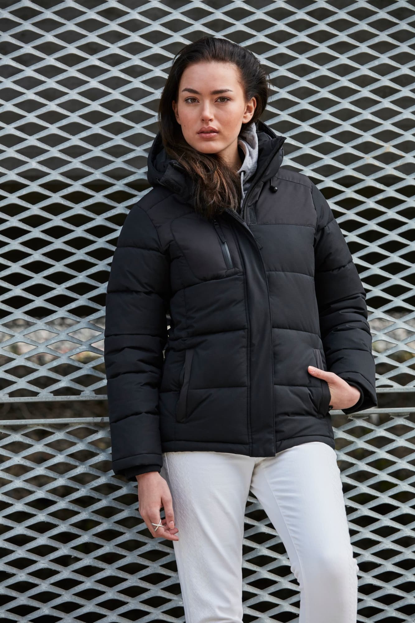 A puffer jacket in black, featuring a zip and hood, displayed on a model against a metal grate background. Ladies Colarado Jacket - Image 1