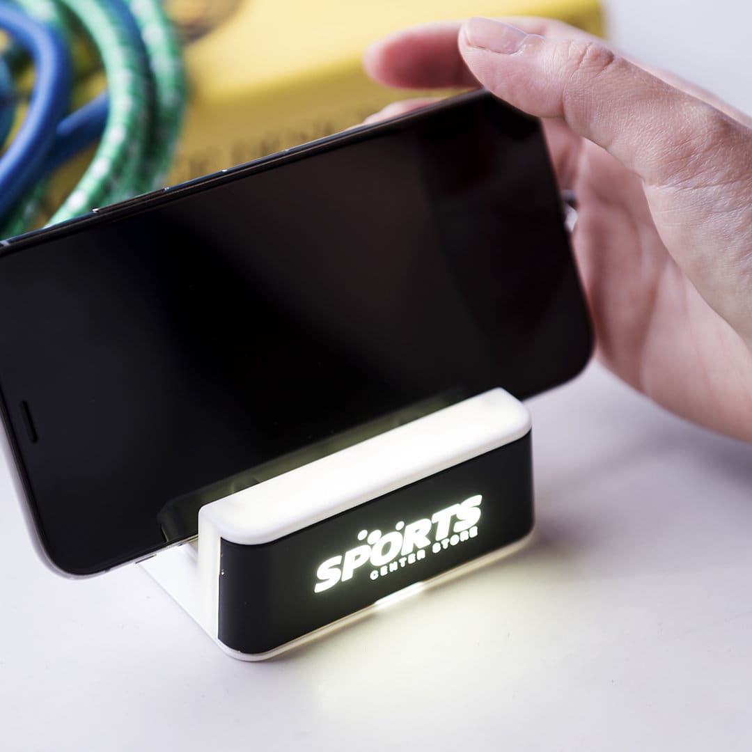 A phone stand with a light, featuring a black base and an illuminated white section, supporting a smartphone. Petrok - Image 1