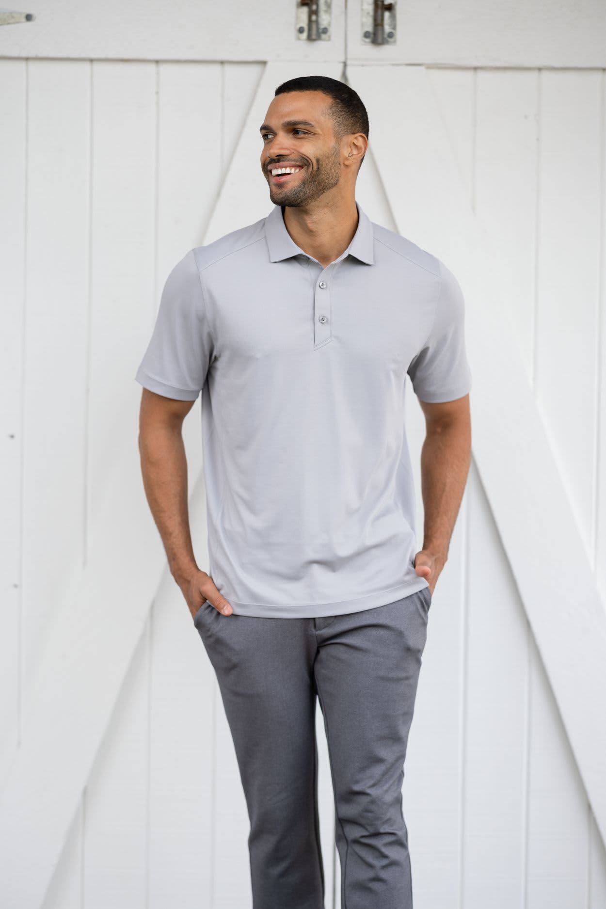 A man wearing a light grey polo shirt with a collar and buttons, paired with grey trousers, standing against a white backdrop. Men’s Forge Eco Polo - Image 1