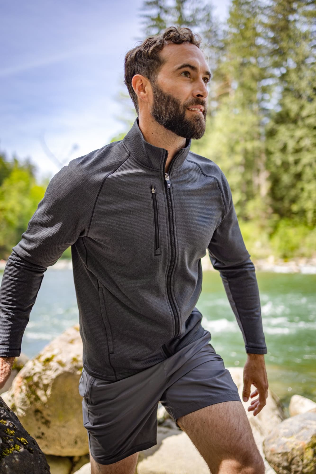 Men’s Peshastin Eco Fleece full zip jacket in dark grey, featuring a front zip pocket, set against a natural river backdrop. Men’s Peshastin Eco Fleece Full Zip - Image 1