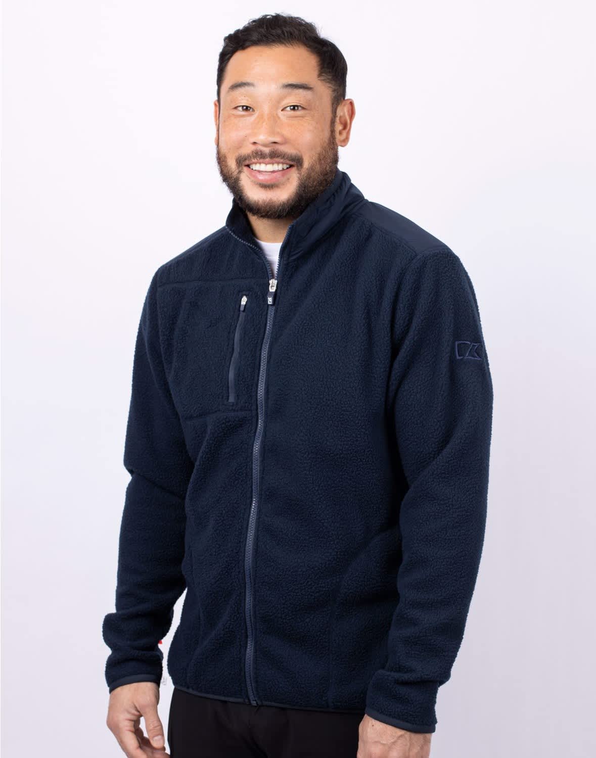 A man wearing a navy blue eco Sherpa jacket with a zippered front and a logo on the sleeve. Men's Cascade Eco Sherpa Jacket - Image 1