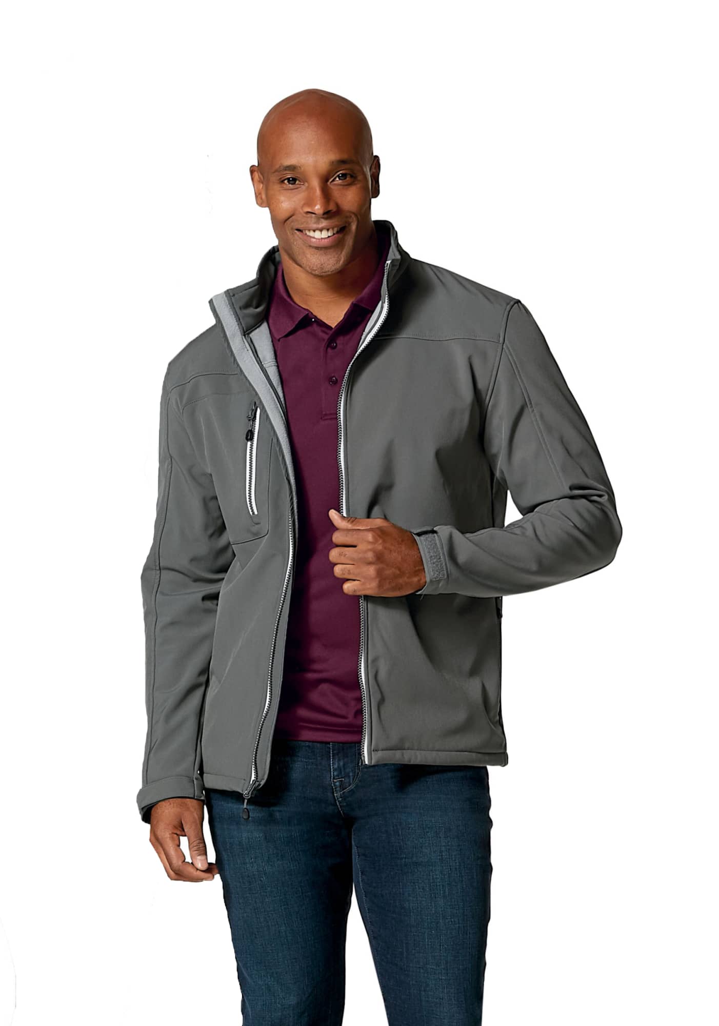 A man models a grey softshell jacket with a zippered pocket and a logo on the chest. He wears a purple polo underneath. Men's Clique Telemark Softshell - Image 1