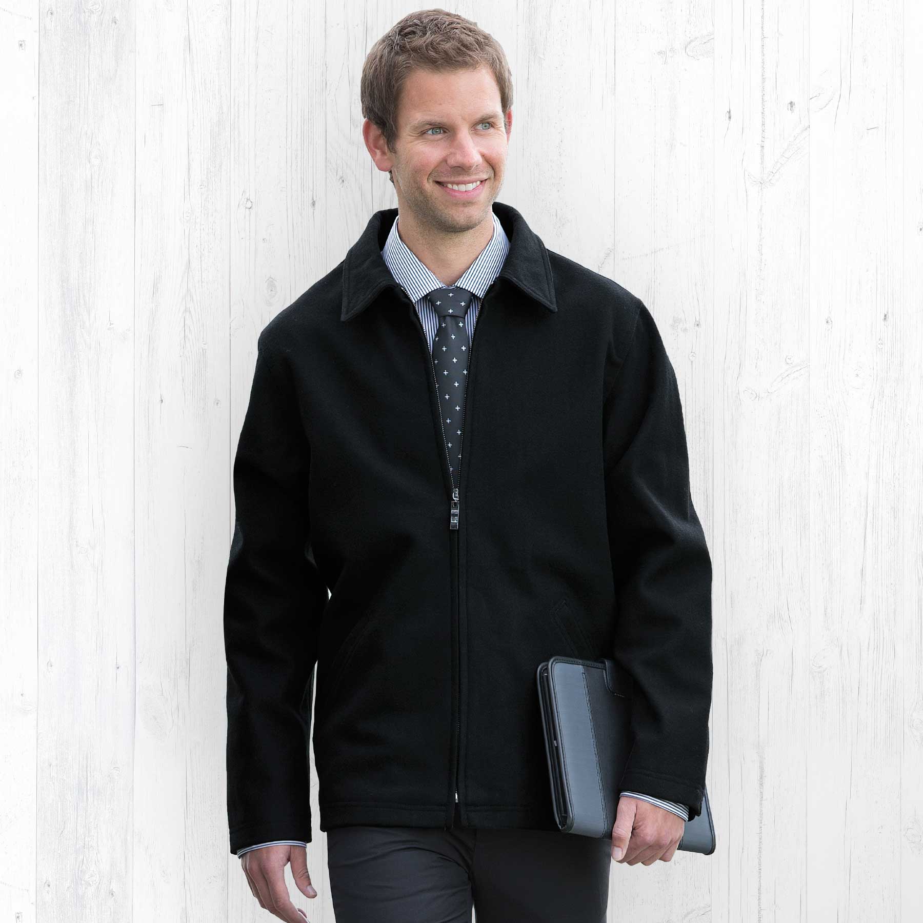 A man in a black Melton wool jacket, holding a laptop, poses against a light wooden background. Melton Wool Ceo Jacket - Mens - Image 1