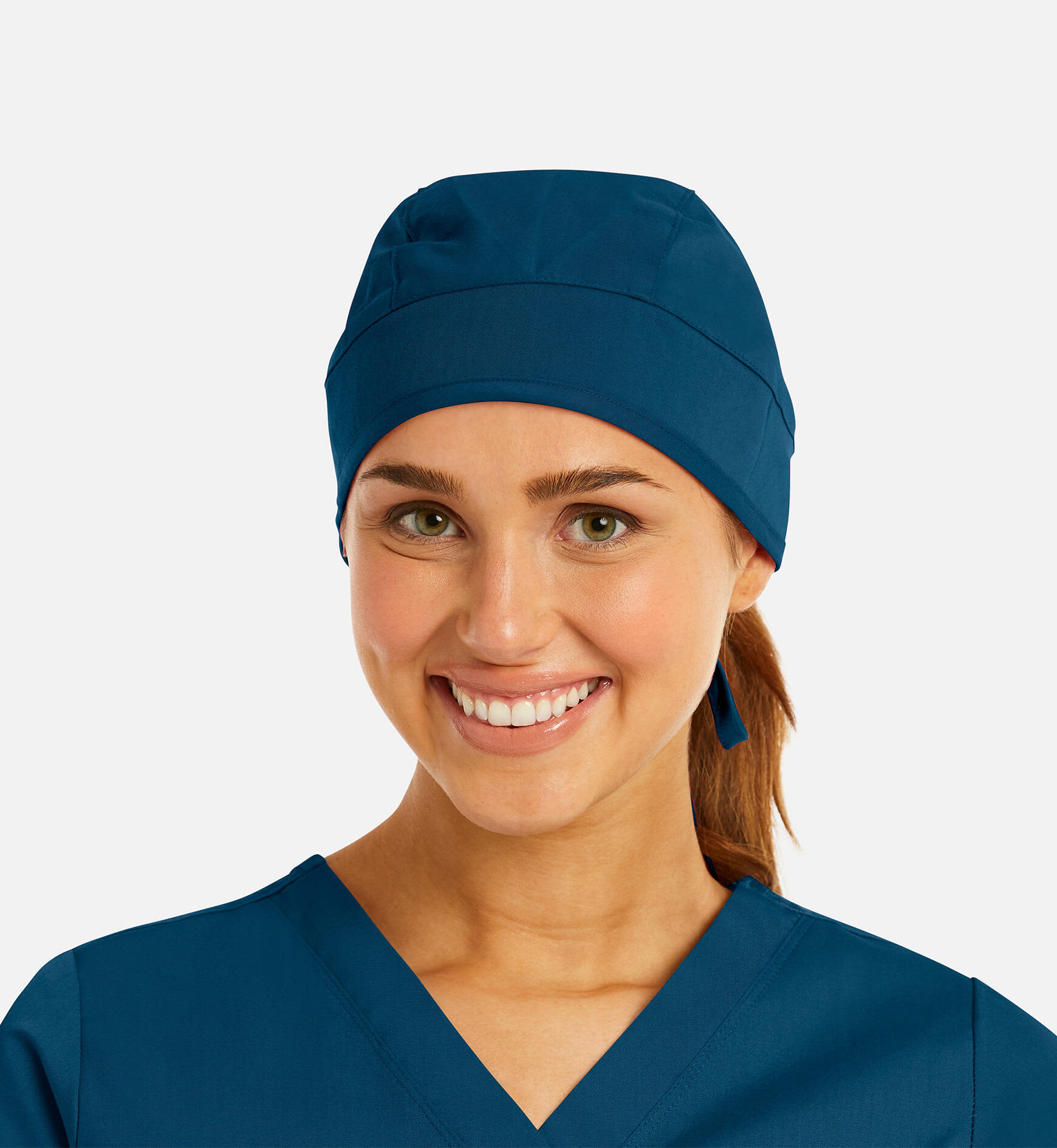 A unisex scrub cap in navy blue, worn by a smiling woman with a ponytail, featuring a logo. Scrub Cap Unisex Cap - Image 1