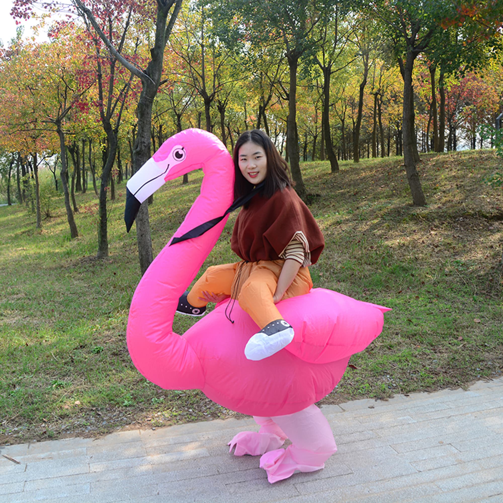 A pink inflatable flamingo costume worn by a person in a park setting with trees and autumn foliage. Halloween Flamingo Inflatable Costume - Image 1