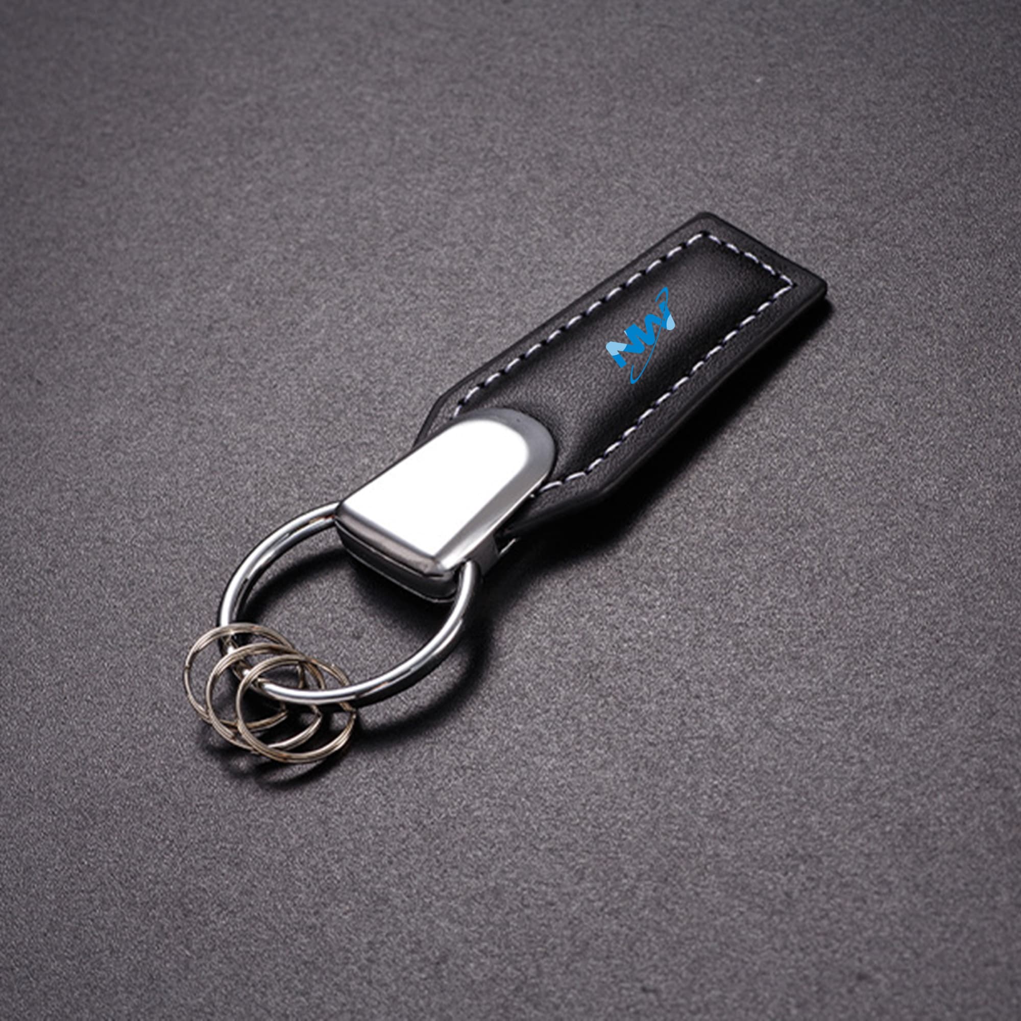 A black leather key chain with a silver keyring and a small logo on the surface. Leather Key Chain - Image 1