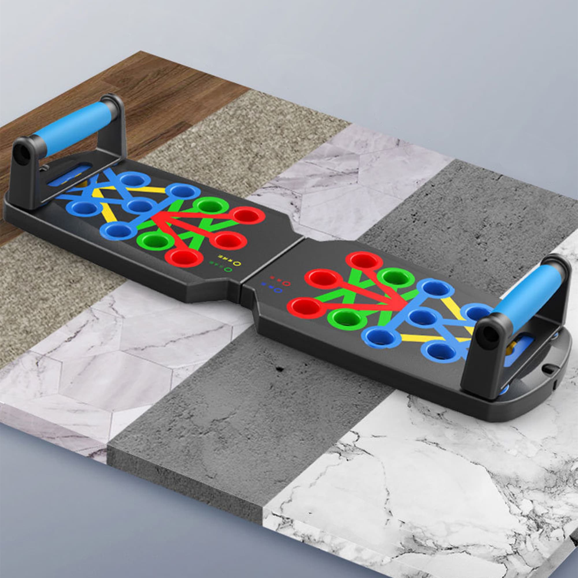 A push-up support board in black with blue handles and multi-coloured holes on a textured surface. Push-up Support Board - Image 1