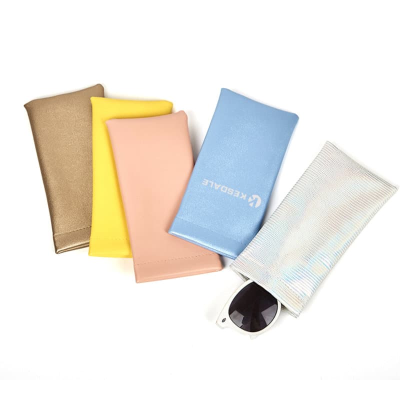 A selection of PVC leather pouches in gold, yellow, pink, blue, and iridescent, with sunglasses partially visible in one. PVC Leather Squeeze Top Glasses Pouch - Image 1