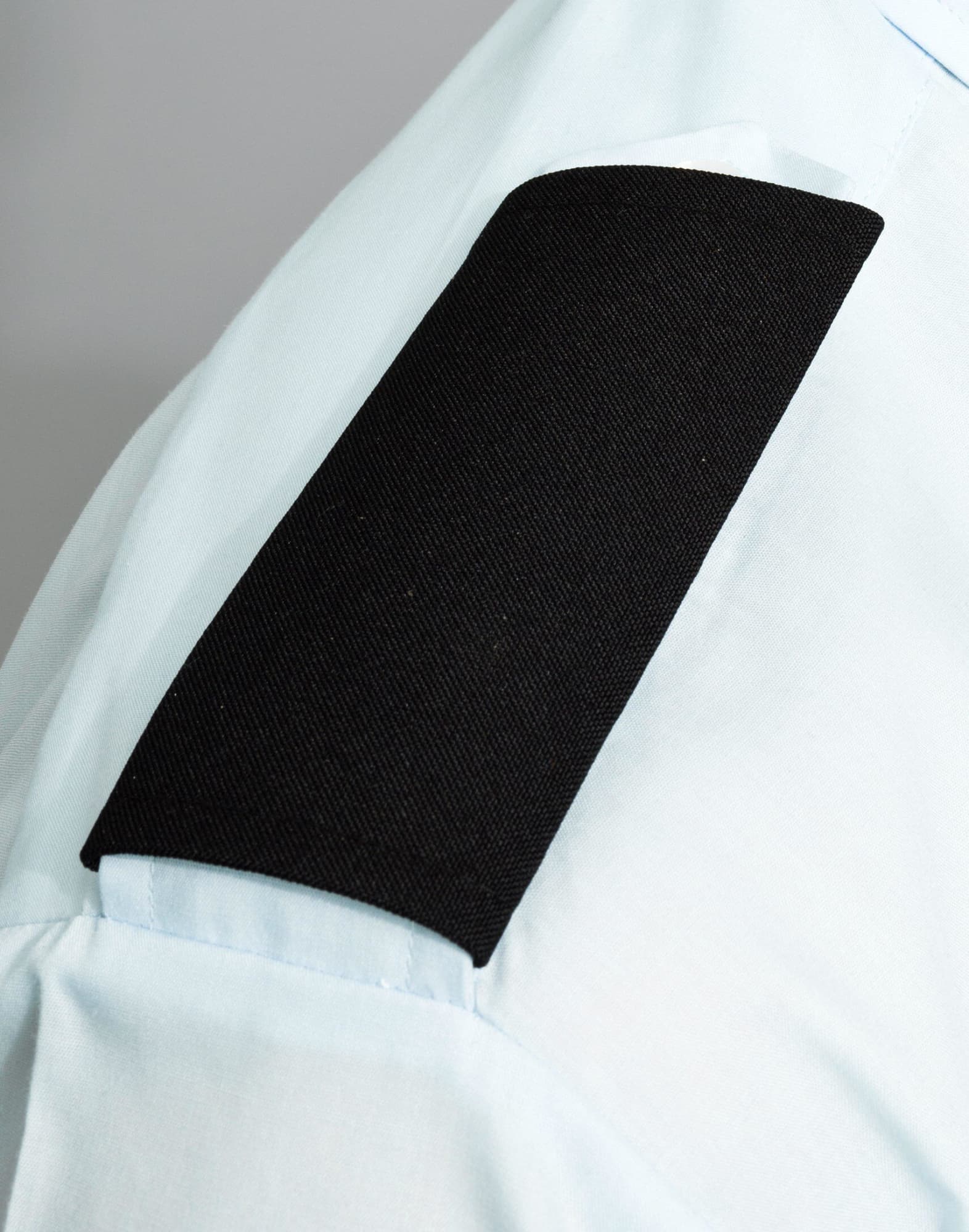 A light blue shirt with a black fabric epaulette on the sleeve, featuring a solid black section. Epaulettes - Image 1