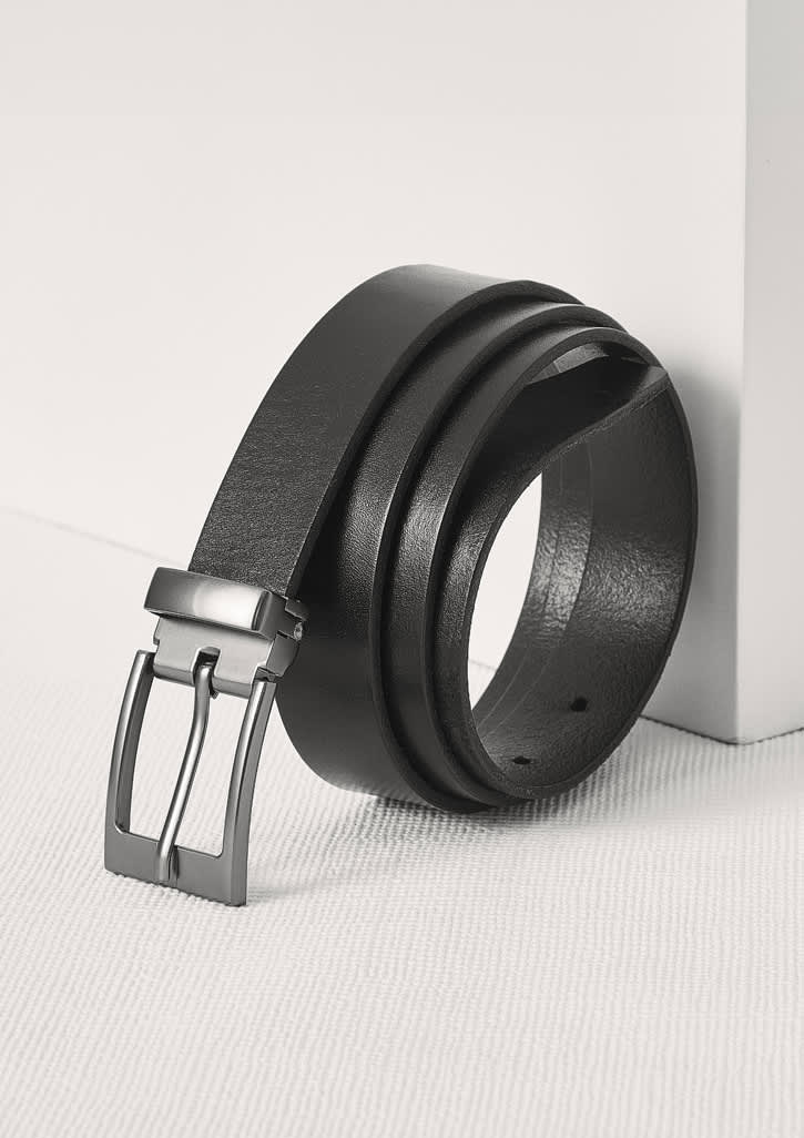 A black leather belt is displayed with a sleek silver buckle, leaning against a white surface. Mens Leather Belt - Image 1