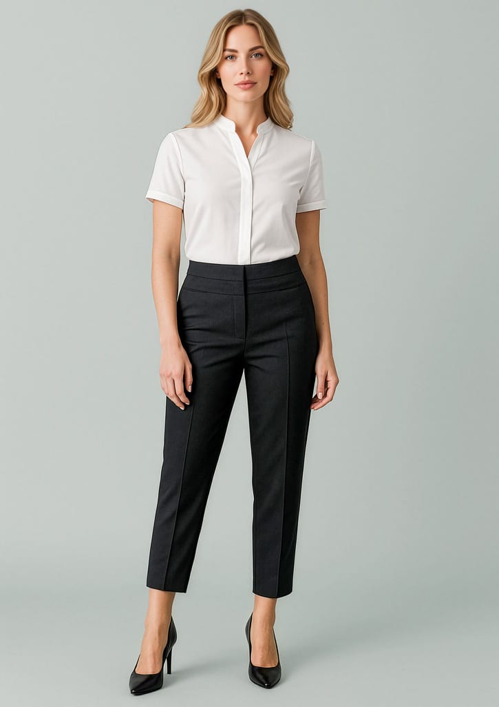 A woman stands wearing a white shirt and black mid-waist slim leg pants with a branding logo, set against a pale background. Womens Renew 7/8 Mid-Waist Slim Leg Pant - Image 1