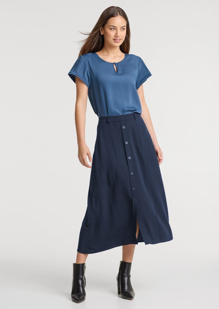 A woman wearing a blue top and a navy skirt with buttons, paired with black ankle boots. The skirt features a front split. Womens Sammy Skirt - Image 1