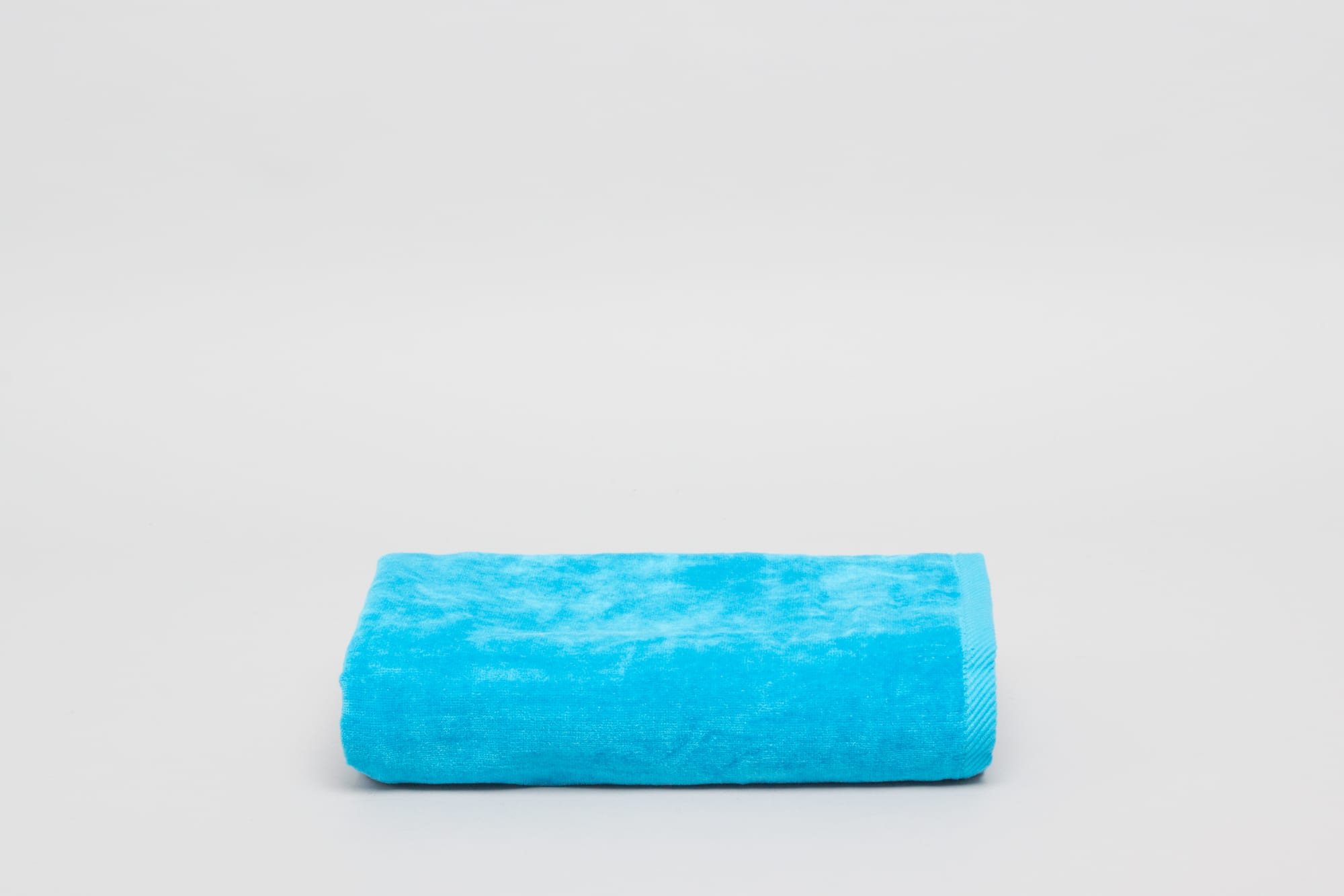 A folded aqua beach pool towel with a textured surface, featuring a bordered edge and a logo. Signature Beach Pool Towel Aqua - Image 1
