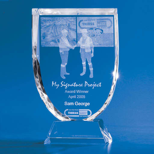 A crystal trophy with a shield shape, featuring two figures shaking hands, set against a blue background. 3D Crystal Shield Trophy - Image 1