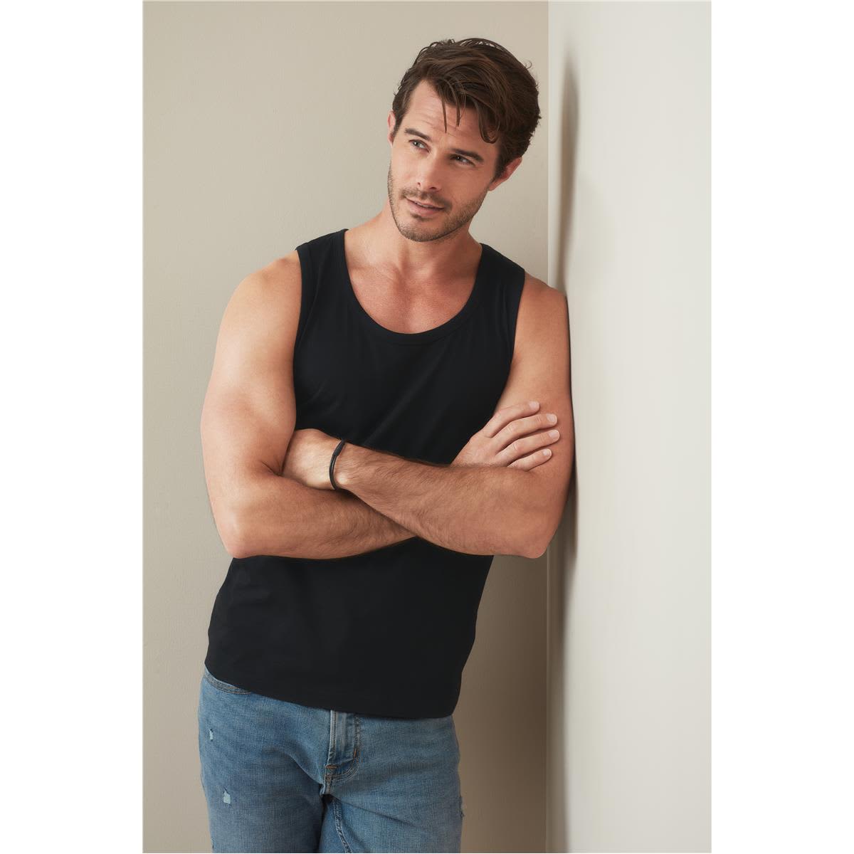 A men's classic tank top in black, displayed by a model leaning against a wall, wearing jeans. Men's Classic Tank Top - Image 1