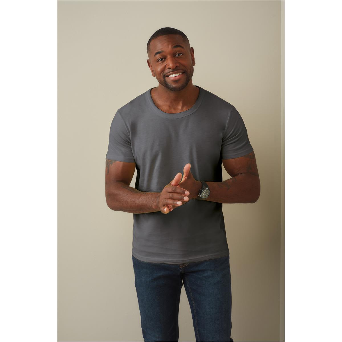 A man wearing a grey crew neck t-shirt and blue jeans, smiling and gesturing with his hands. Men's Ben Crew Neck - Image 1