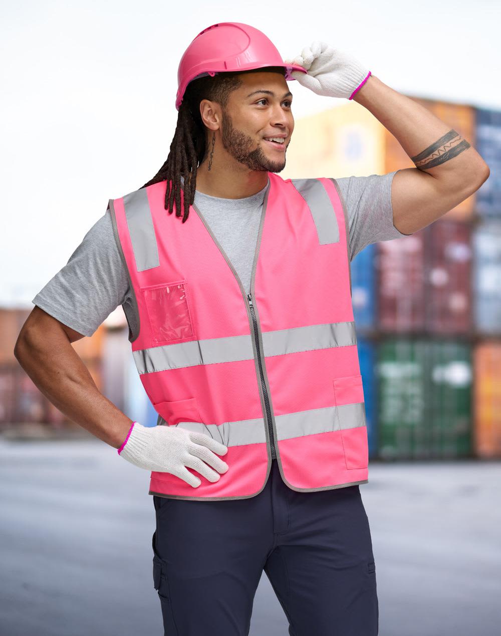 A pink high-visibility safety zip vest with reflective stripes, worn by a person in a grey shirt and pink helmet. Hi Vis Safety Zip Vest With ID & Utility Pockets - Image 1