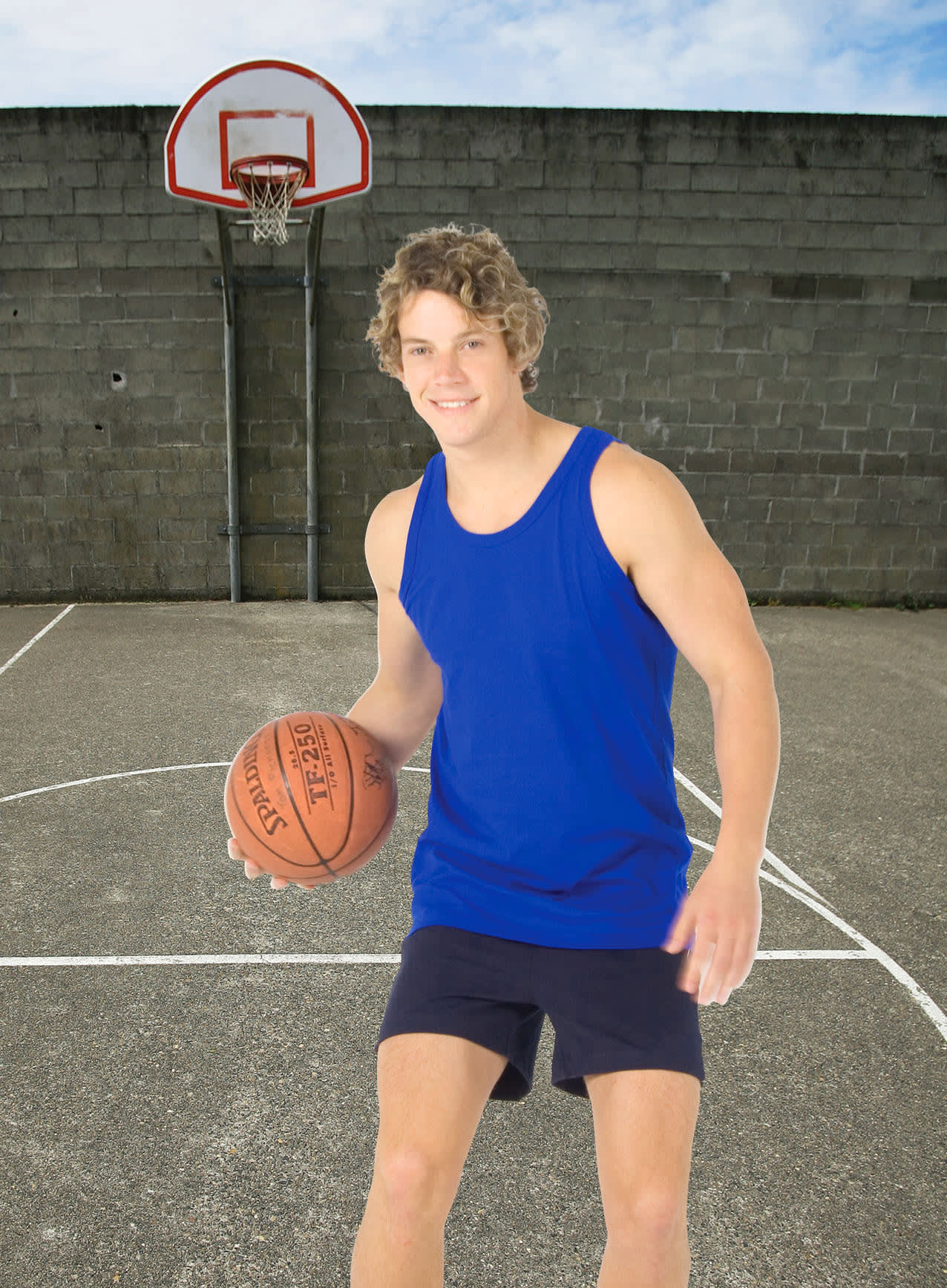 A young man in a blue cotton singlet and shorts holds a basketball on an outdoor court with a hoop in the background. Men's Cotton Singlet - Image 1