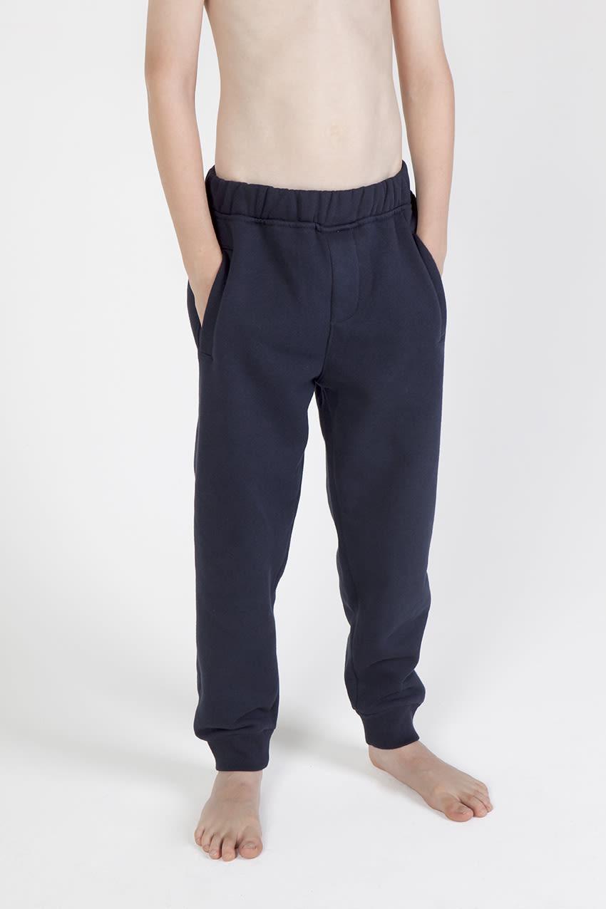 Junior track pants in navy, featuring an elastic waistband and side pockets, displayed on a bare torso. Junior Track Pants - Image 1