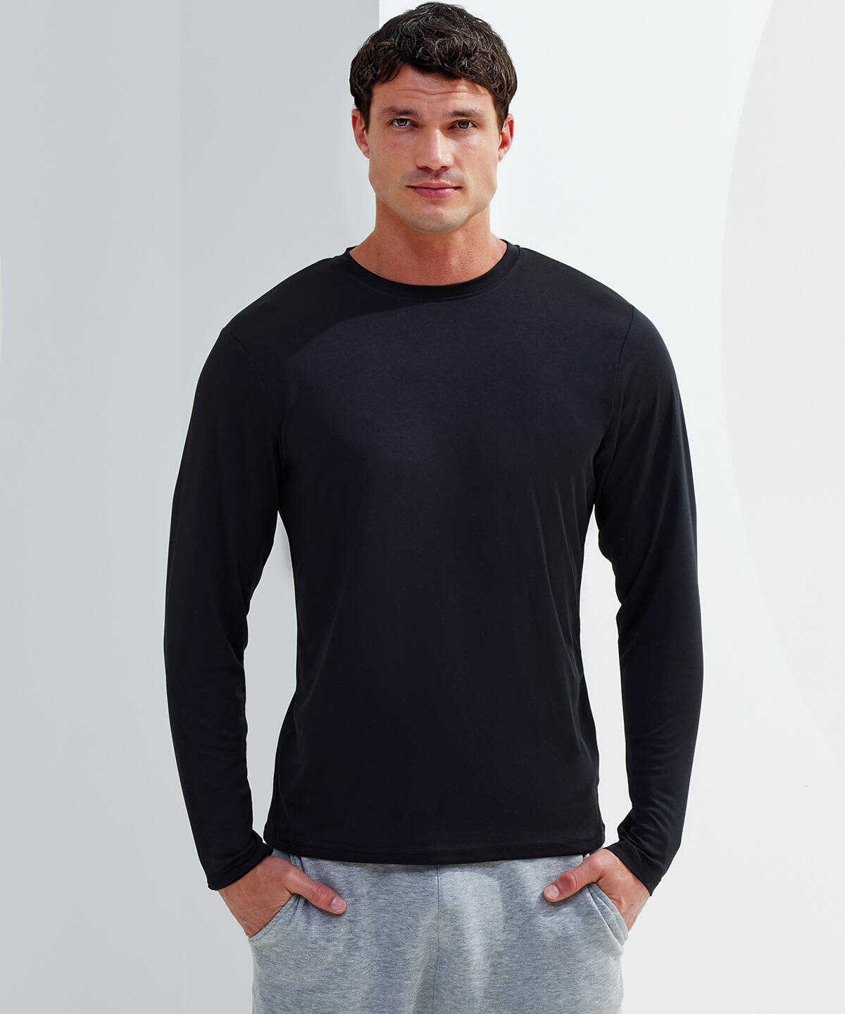A long sleeve performance t-shirt in black, worn by a model, paired with grey pants. The shirt features a logo. Long Sleeve Performance T-Shirt - Image 1