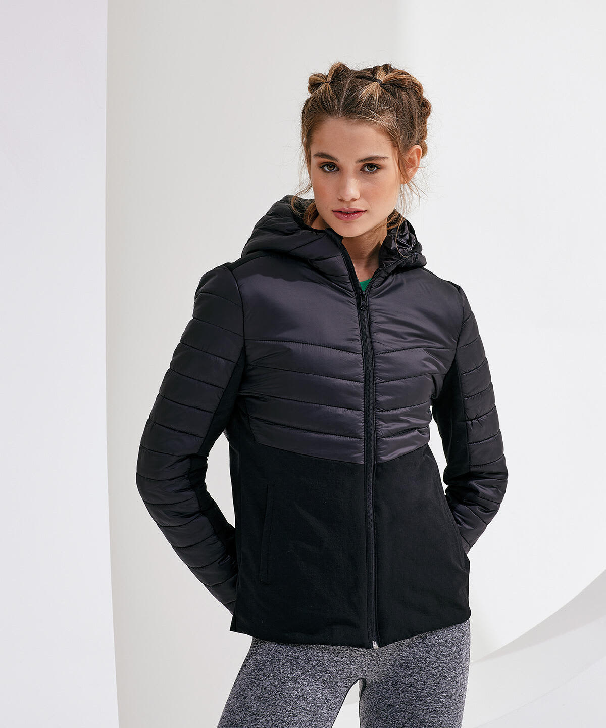 A woman wearing a black insulated hybrid jacket with a hood, featuring quilted panels and a sleek design. Insulated Hybrid Jacket - Image 1
