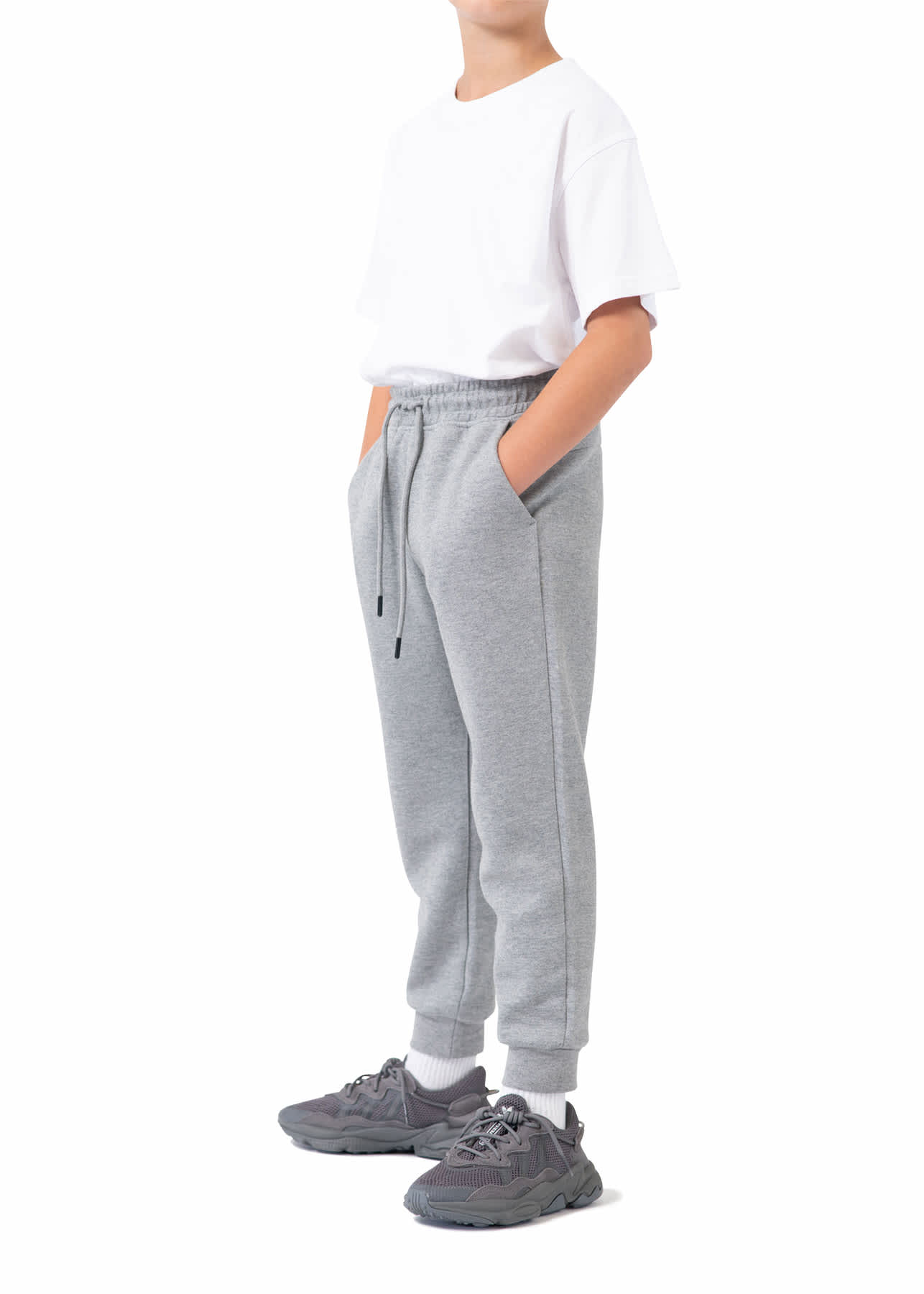 Grey three-layer cotton track pants with pockets, worn by a child in a white t-shirt and athletic shoes. Kids's three layer Cotton Sandwich Pants - Image 1