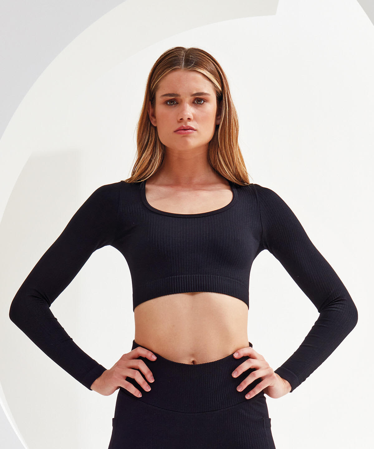 A ribbed, seamless black crop top with long sleeves and a scoop neckline. It features a fitted design and has a logo. Ribbed Seamless 3D Fit Crop Top - Image 1