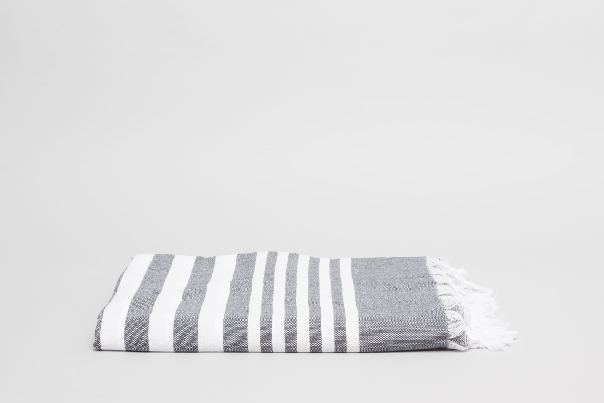A folded charcoal grey beach and pool towel with white stripes and fringed edges. Turkish Beach & Pool Towel 400 gsm Charcoal - Image 1