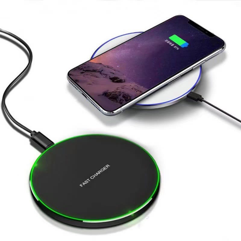 A black wireless charging pad with a green light, positioned next to a smartphone displaying a charging icon. 15W Light Up Wireless Charging Pad - Image 1