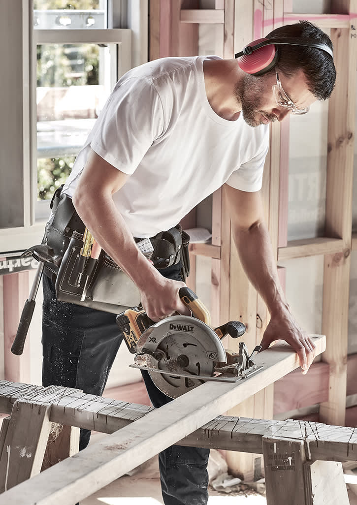 A man in a white T-shirt uses a circular saw on a wooden plank, wearing safety glasses and noise-cancelling headphones. Mens Streetworx Tee - Image 1