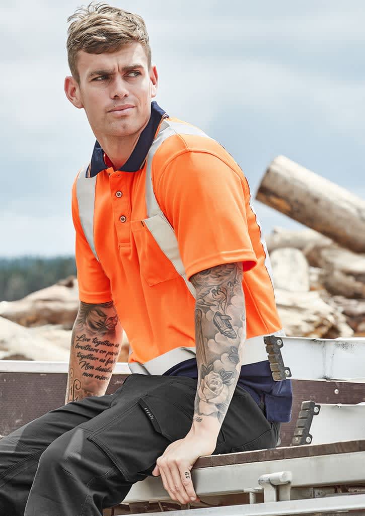 An orange short sleeve polo shirt with shoulder tape detail, worn by a tattooed man sitting outdoors. Mens Hi Vis Spliced Short Sleeve Polo - Shoulder Taped - Image 1