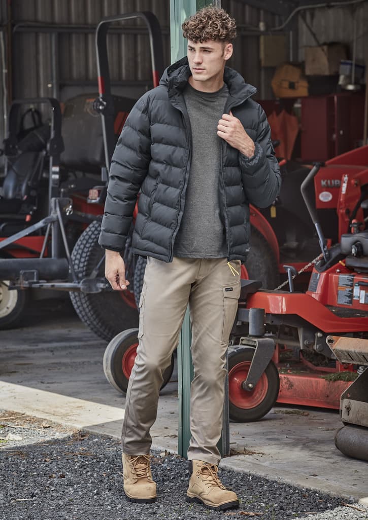 A black hooded puffer jacket is worn over a grey shirt, paired with beige pants and tan boots in an outdoor setting. Unisex Streetworx Hooded Puffer Jacket - Image 1