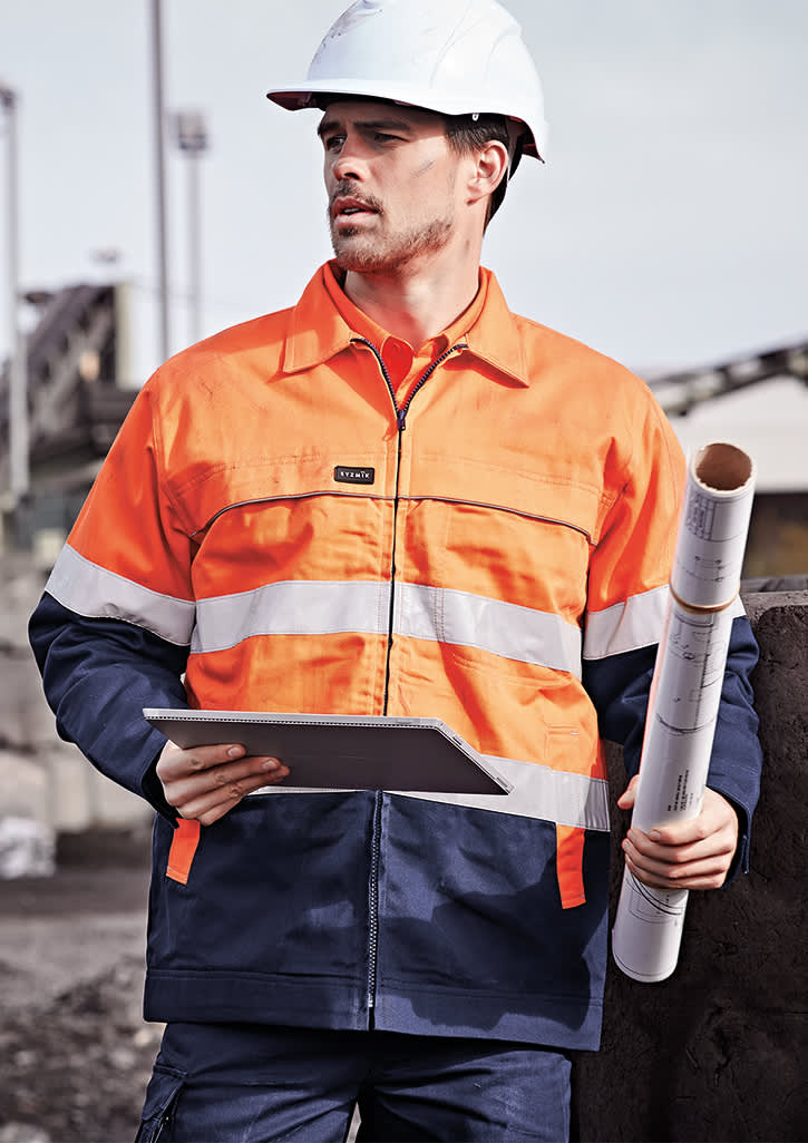 A man wearing a men's hi-vis cotton drill jacket in orange and navy, holding a blueprint and wearing a helmet. Mens Hi Vis Cotton Drill Jacket - Image 1