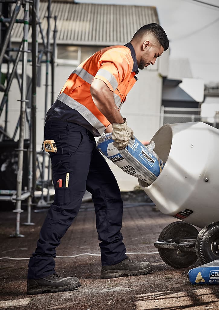 A man in orange and grey high-visibility workwear pours from a bag into a mixer, wearing navy rugged cargo pants. Mens Rugged Cooling Cargo Pant (Regular) - Image 1