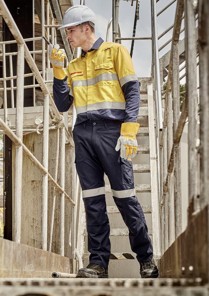 A worker in a yellow and navy work shirt and cargo pants, wearing gloves and a hard hat, on a metal staircase. Mens Orange Flame Taped Cargo Pant (Stout) - Image 1