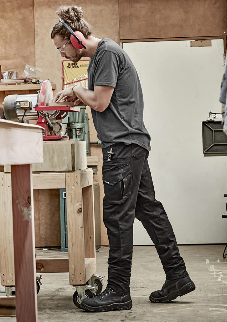 Men's rugged cooling stretch pants in black, featuring cargo pockets, are worn by a person working in a workshop. Mens Rugged Cooling Stretch Pant - Image 1